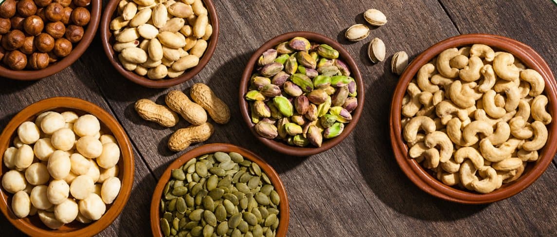 Bowls of cashews, hazelnuts, pistachios, peanuts, macadamias and pumpkin seeds on a wooden table