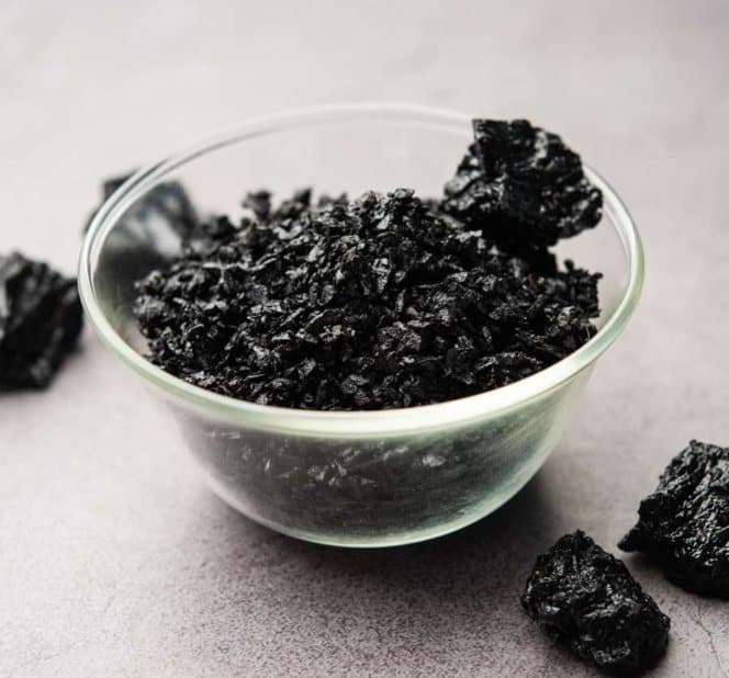 Glass bowl of dark organic mineral pieces on a grey stone surface