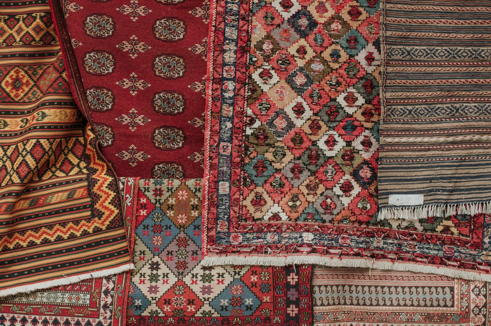 Stacks of hand-knotted Afghan carpets with red and ivory tribal patterns